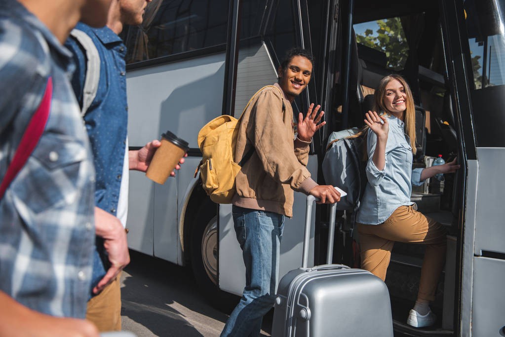 stock-photo-happy-multiethnic-tourists-backpacks-wheeled-bags-waving-hands-friends-while